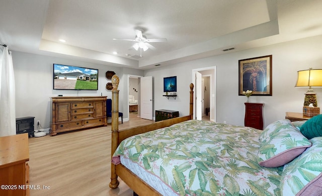 bedroom with a raised ceiling, ensuite bathroom, ceiling fan, and hardwood / wood-style flooring