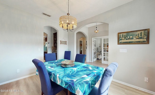 dining area featuring wood-type flooring, an inviting chandelier, and french doors