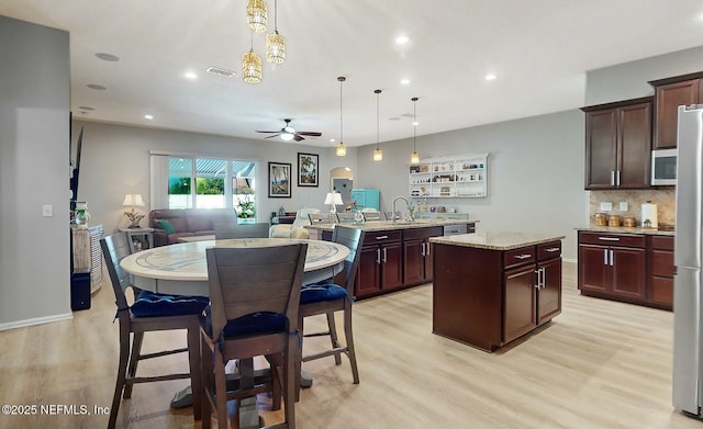 kitchen with ceiling fan, a center island, light stone countertops, light hardwood / wood-style flooring, and decorative light fixtures