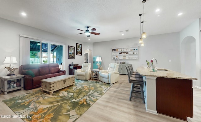 living room featuring a textured ceiling, ceiling fan, light wood-type flooring, and sink