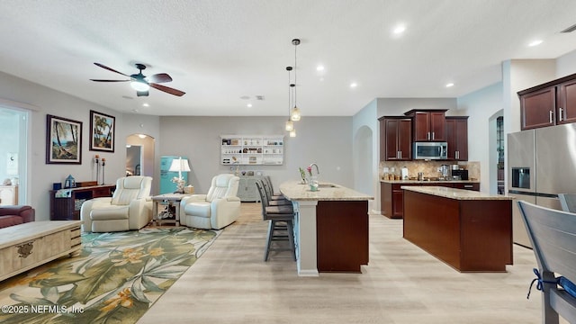 kitchen featuring pendant lighting, a breakfast bar area, appliances with stainless steel finishes, an island with sink, and decorative backsplash