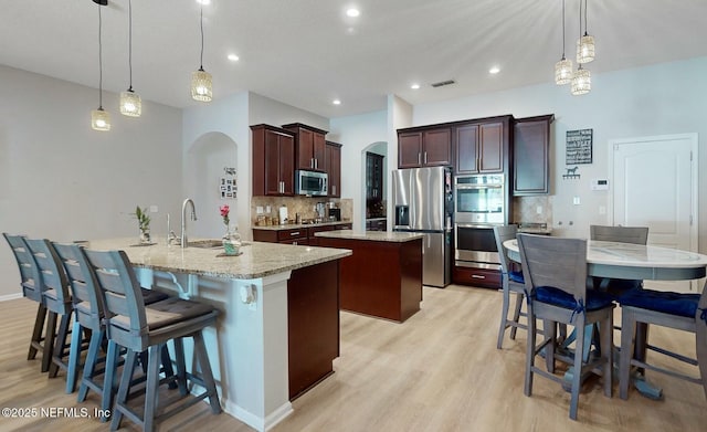 kitchen with backsplash, stainless steel appliances, hanging light fixtures, and a center island with sink