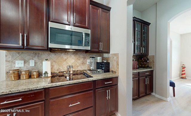 kitchen with decorative backsplash, light stone countertops, black electric stovetop, and light hardwood / wood-style floors