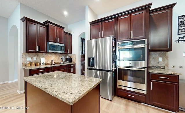 kitchen featuring light stone counters, decorative backsplash, stainless steel appliances, and a kitchen island