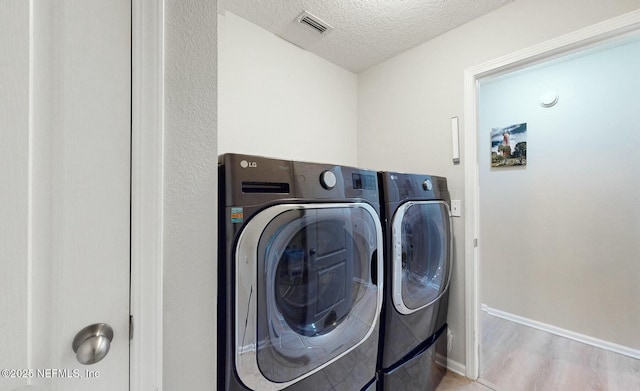 laundry room featuring washing machine and dryer, light wood-type flooring, and a textured ceiling