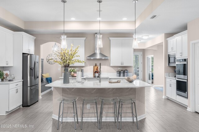 kitchen with white cabinets, hanging light fixtures, wall chimney range hood, and appliances with stainless steel finishes