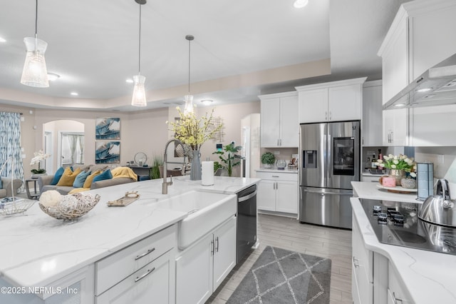 kitchen with white cabinets, wall chimney range hood, appliances with stainless steel finishes, and a tray ceiling