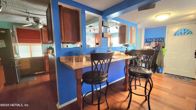 bar with ceiling fan, beamed ceiling, refrigerator, wood-type flooring, and a textured ceiling