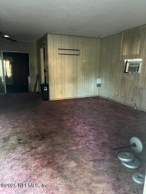 unfurnished living room featuring cooling unit, wooden walls, and dark carpet