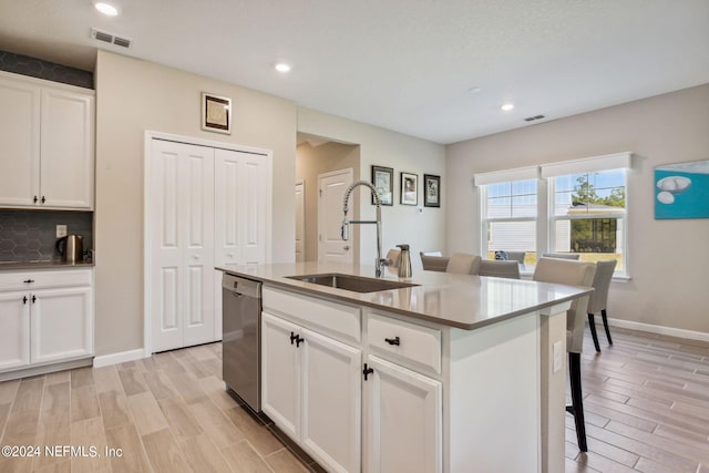 kitchen with a center island with sink, white cabinets, sink, stainless steel dishwasher, and a kitchen bar