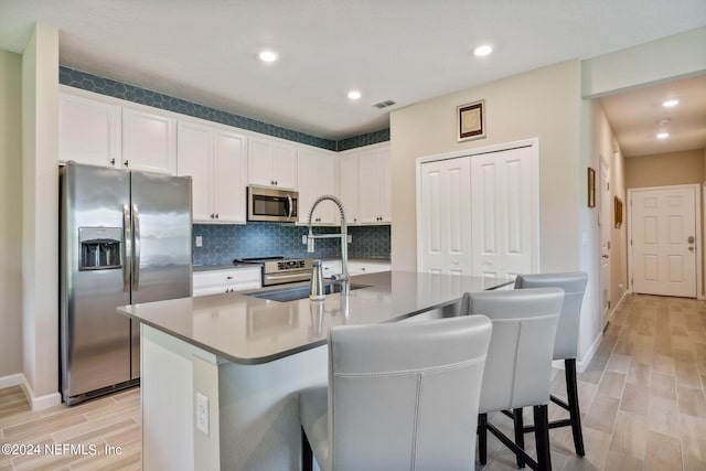 kitchen with a breakfast bar area, white cabinetry, a center island with sink, and appliances with stainless steel finishes