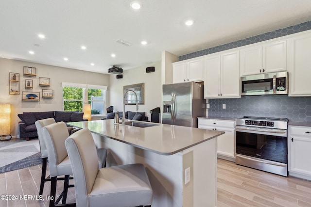 kitchen featuring appliances with stainless steel finishes, a kitchen breakfast bar, sink, white cabinetry, and an island with sink