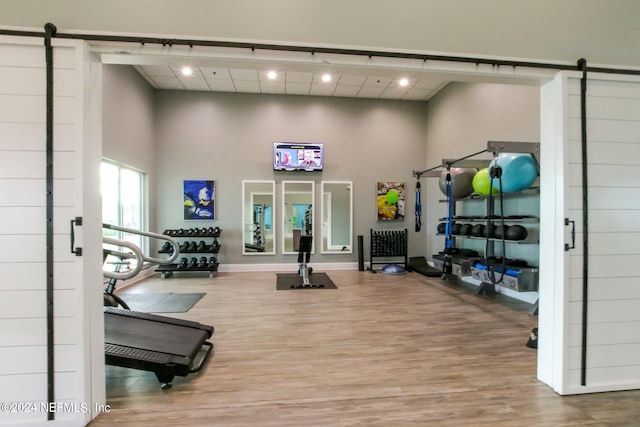 exercise room featuring a barn door, wood-type flooring, and a towering ceiling