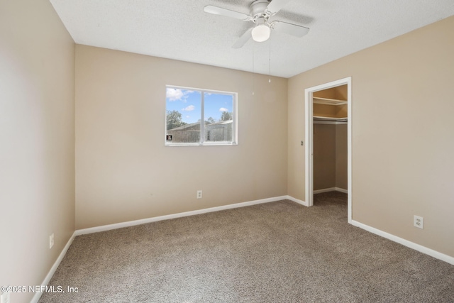 unfurnished bedroom with a walk in closet, ceiling fan, a closet, and carpet