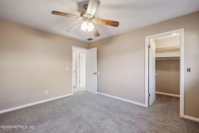 unfurnished bedroom with carpet, a walk in closet, a textured ceiling, ceiling fan, and a closet