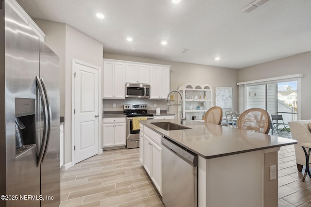 kitchen with white cabinets, appliances with stainless steel finishes, a center island with sink, and sink