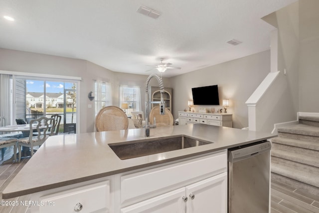 kitchen with ceiling fan, sink, dishwasher, white cabinetry, and an island with sink