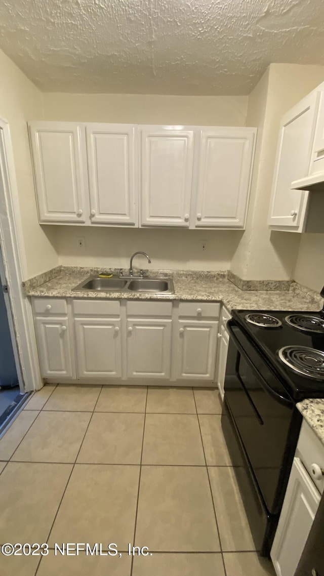 kitchen with light stone counters, sink, light tile patterned floors, electric range, and white cabinets