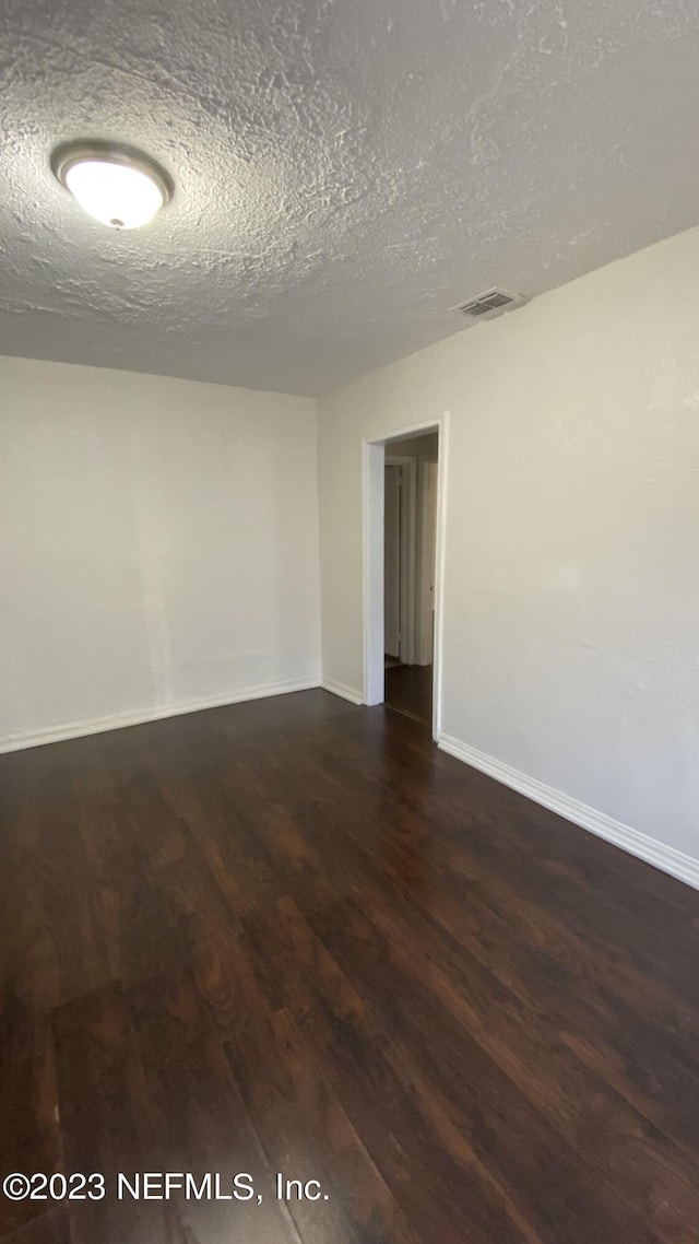 spare room featuring a textured ceiling and dark hardwood / wood-style floors