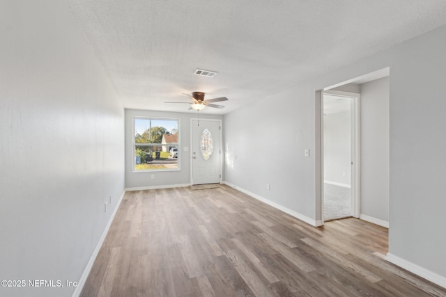 unfurnished room featuring light wood-style floors, baseboards, visible vents, and a textured ceiling