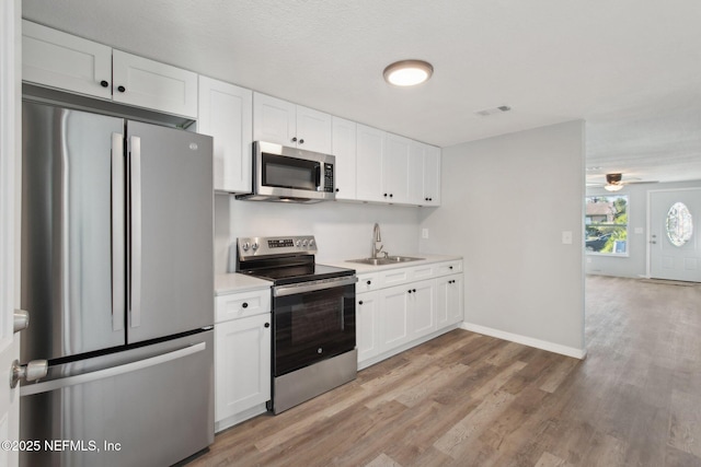 kitchen featuring light wood-style flooring, stainless steel appliances, a sink, white cabinets, and light countertops