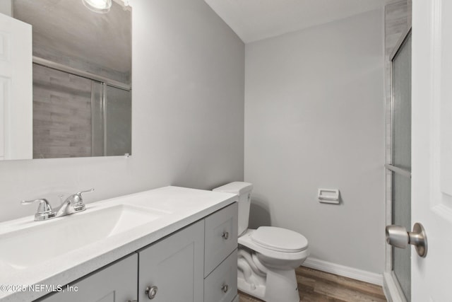 bathroom with toilet, wood finished floors, vanity, baseboards, and an enclosed shower