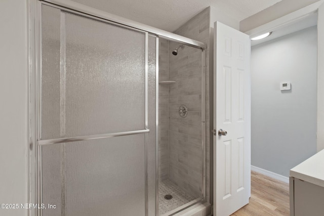 full bath featuring a shower stall, baseboards, and wood finished floors