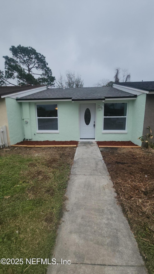 view of front of property featuring a shingled roof, a front lawn, and stucco siding