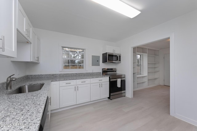 kitchen with white cabinetry, sink, light stone countertops, light hardwood / wood-style floors, and appliances with stainless steel finishes