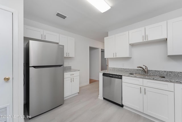 kitchen with appliances with stainless steel finishes, light stone counters, sink, white cabinets, and light hardwood / wood-style floors