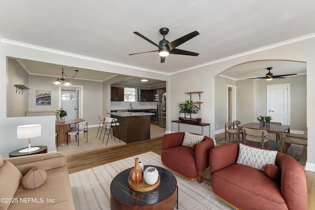 living room with ceiling fan with notable chandelier, ornamental molding, and light hardwood / wood-style floors