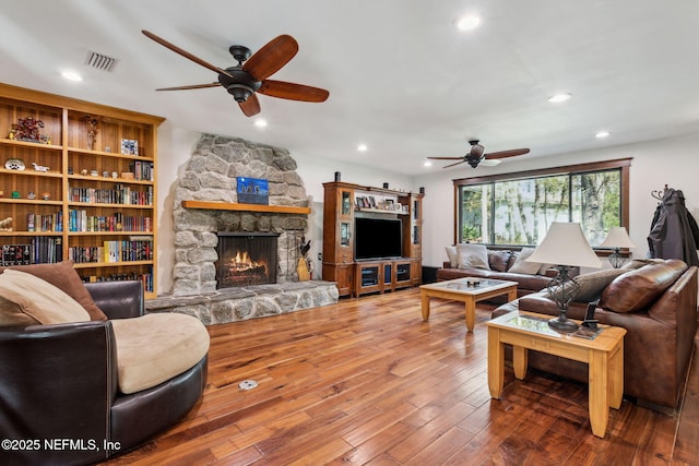 living room with a stone fireplace, ceiling fan, and hardwood / wood-style floors