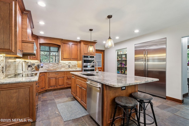 kitchen featuring appliances with stainless steel finishes, backsplash, a kitchen island with sink, sink, and pendant lighting