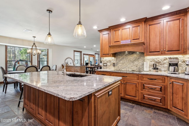 kitchen with sink, pendant lighting, a chandelier, a kitchen bar, and a kitchen island with sink