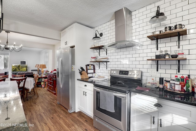 kitchen with an inviting chandelier, wall chimney exhaust hood, decorative backsplash, white cabinetry, and stainless steel appliances