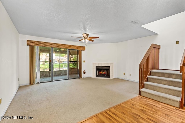 unfurnished living room featuring a tile fireplace, ceiling fan, light hardwood / wood-style floors, and a textured ceiling