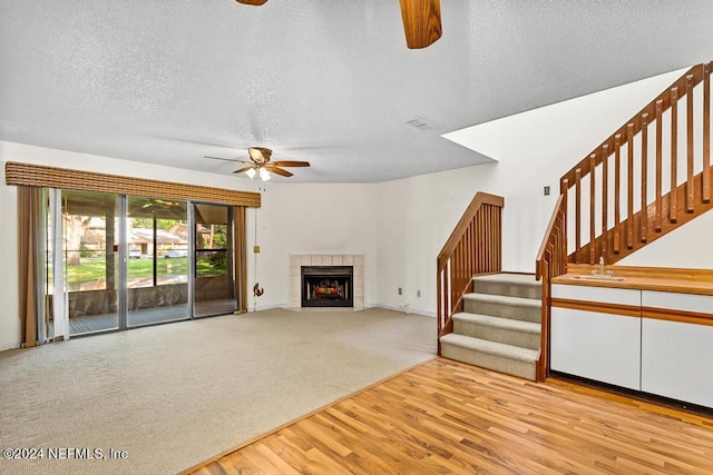 unfurnished living room featuring sink, ceiling fan, light wood-type flooring, a textured ceiling, and a tiled fireplace