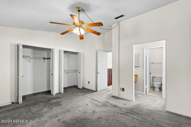 unfurnished bedroom with two closets, carpet flooring, ceiling fan, a towering ceiling, and connected bathroom