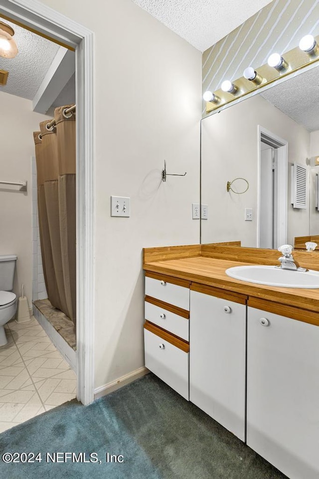 bathroom with vanity, toilet, a textured ceiling, and walk in shower