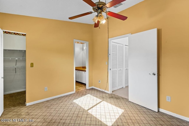 unfurnished bedroom with ceiling fan, ensuite bathroom, light colored carpet, vaulted ceiling, and a walk in closet