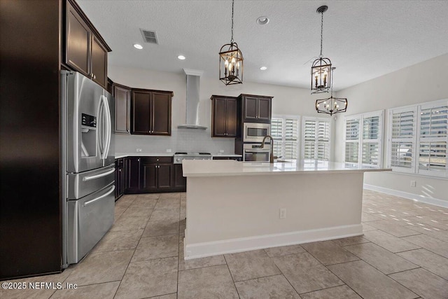 kitchen with a kitchen island with sink, an inviting chandelier, wall chimney exhaust hood, decorative light fixtures, and stainless steel appliances