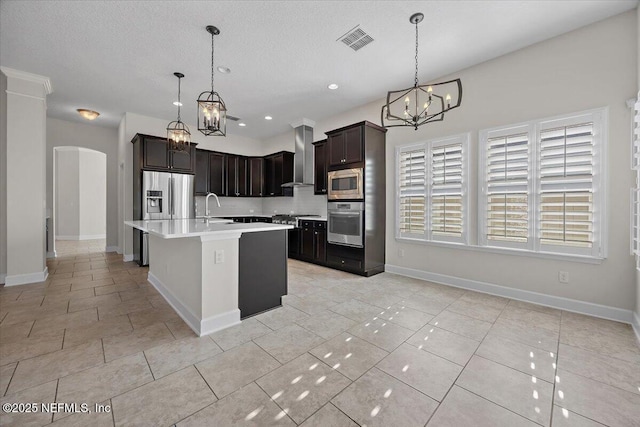 kitchen featuring a center island with sink, hanging light fixtures, wall chimney range hood, and appliances with stainless steel finishes