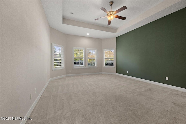 empty room featuring ceiling fan, light colored carpet, and a tray ceiling