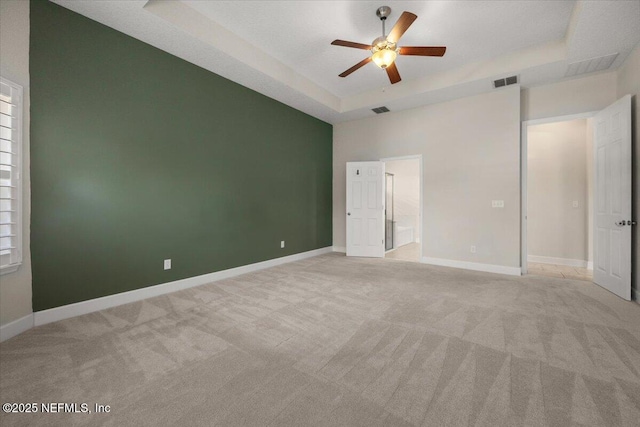 unfurnished bedroom with ceiling fan, light carpet, and a tray ceiling