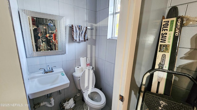 bathroom with a sink, toilet, and tile walls