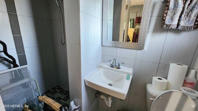 bathroom with a stall shower, toilet, tile walls, and a sink