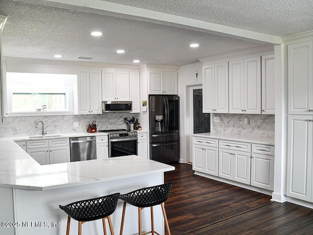 kitchen featuring dark wood-style flooring, a sink, stainless steel appliances, white cabinets, and a kitchen breakfast bar