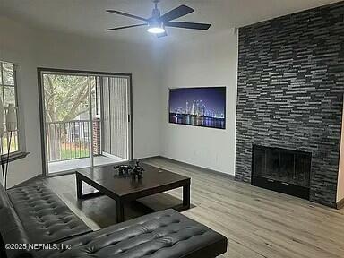 living room with ceiling fan, a healthy amount of sunlight, a stone fireplace, and wood-type flooring