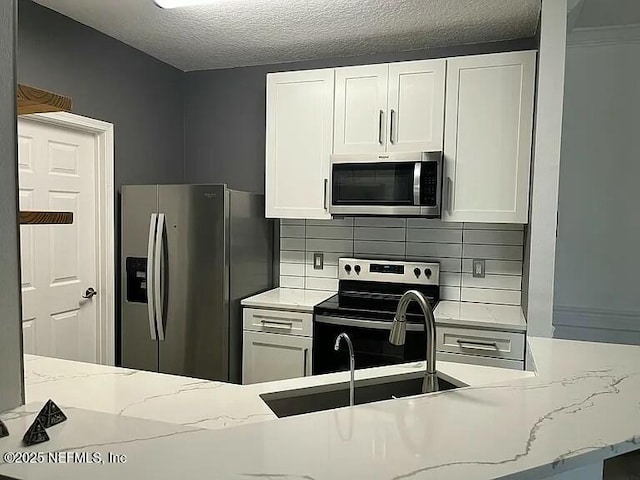 kitchen with white cabinetry, sink, stainless steel appliances, light stone counters, and a textured ceiling