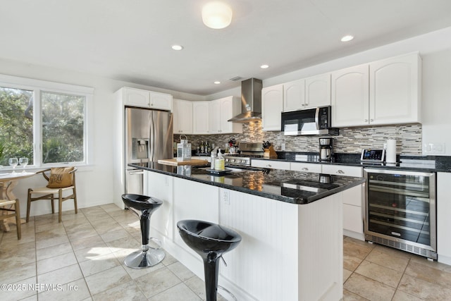 kitchen featuring a breakfast bar, wall chimney exhaust hood, a kitchen island, white cabinetry, and beverage cooler